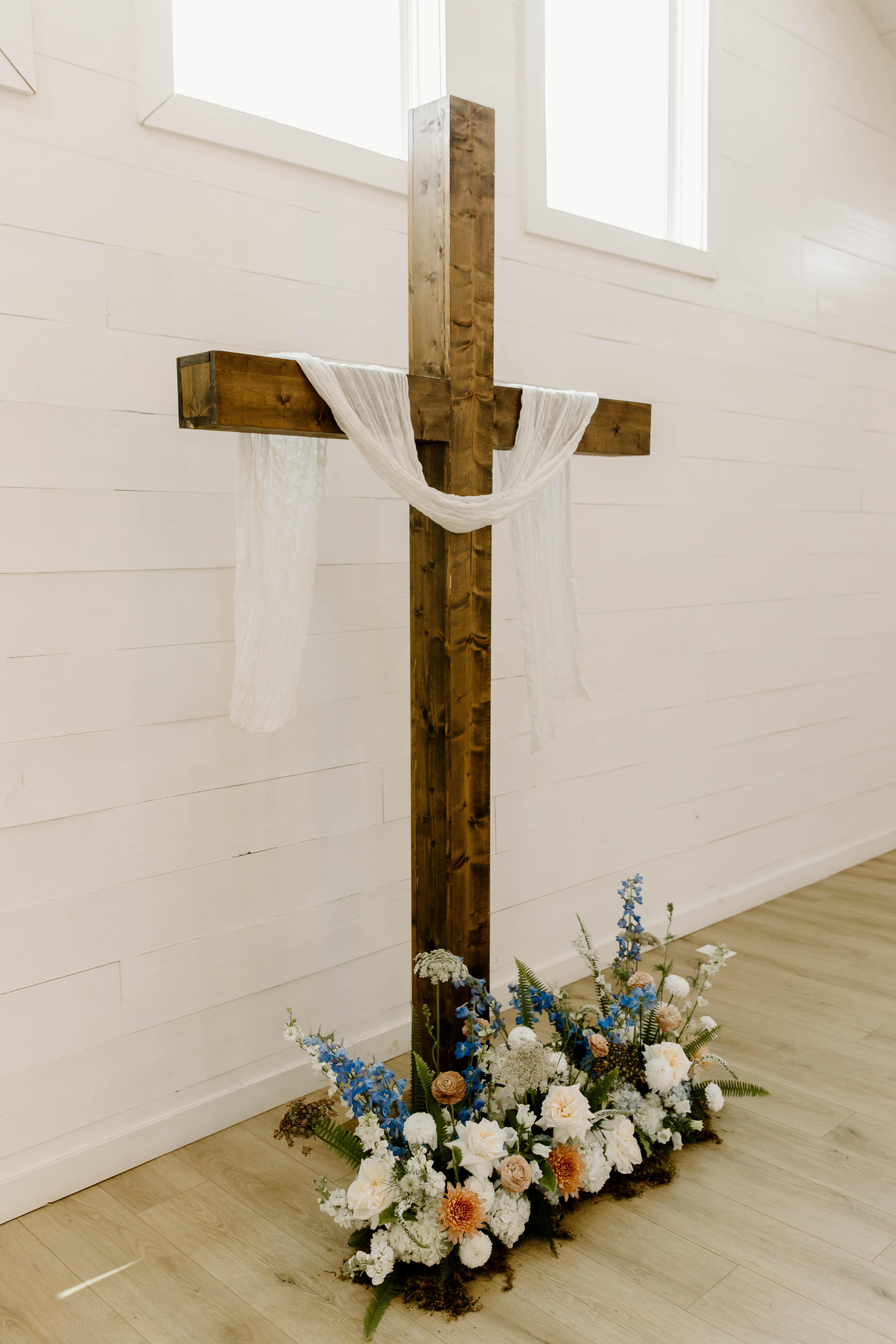 A wooden ceremony cross with white draping and blue, white, and peach flowers at Brooke’s wedding