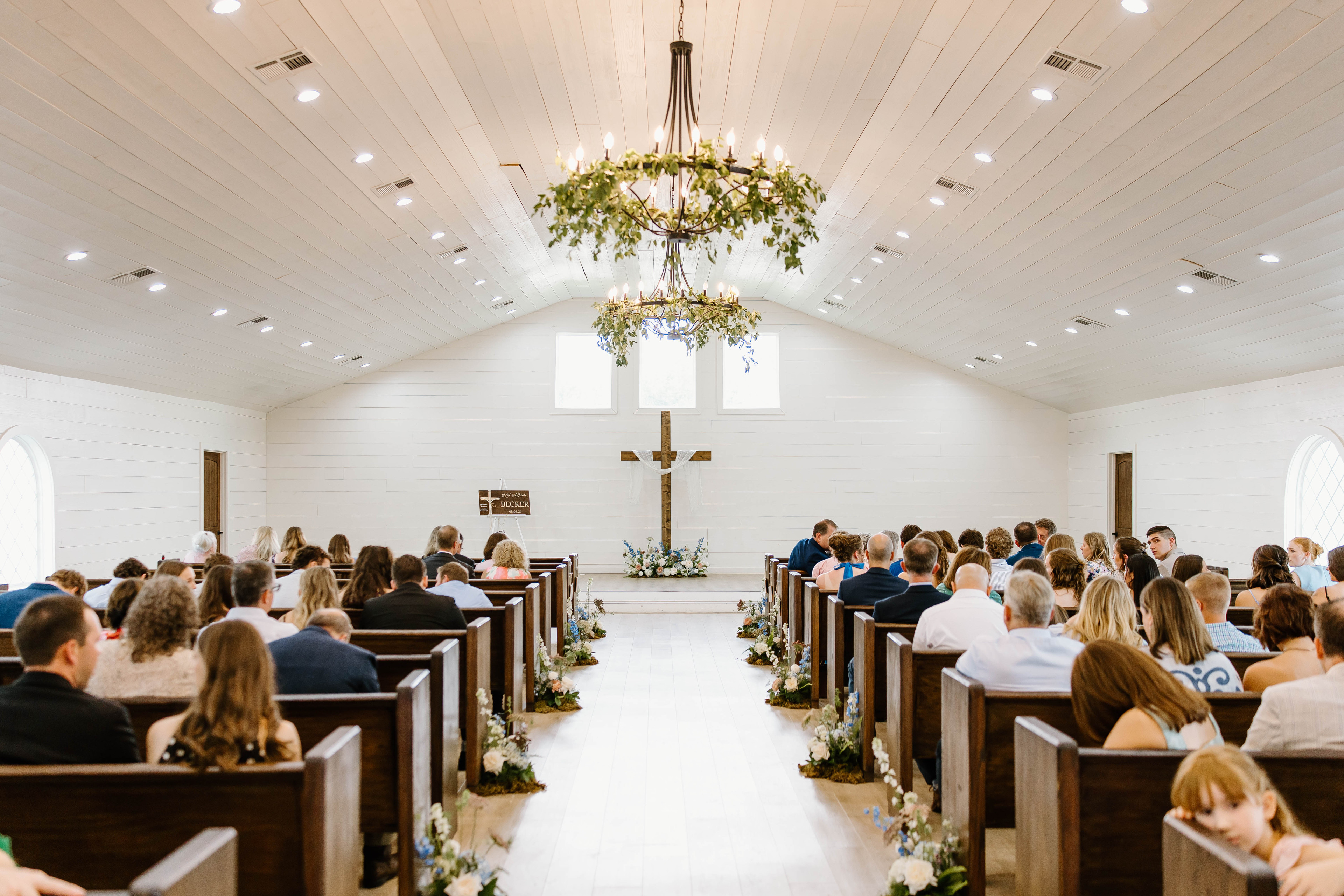 Brooke’s chapel ceremony with floral aisle arrangements and greenery on the chandeliers