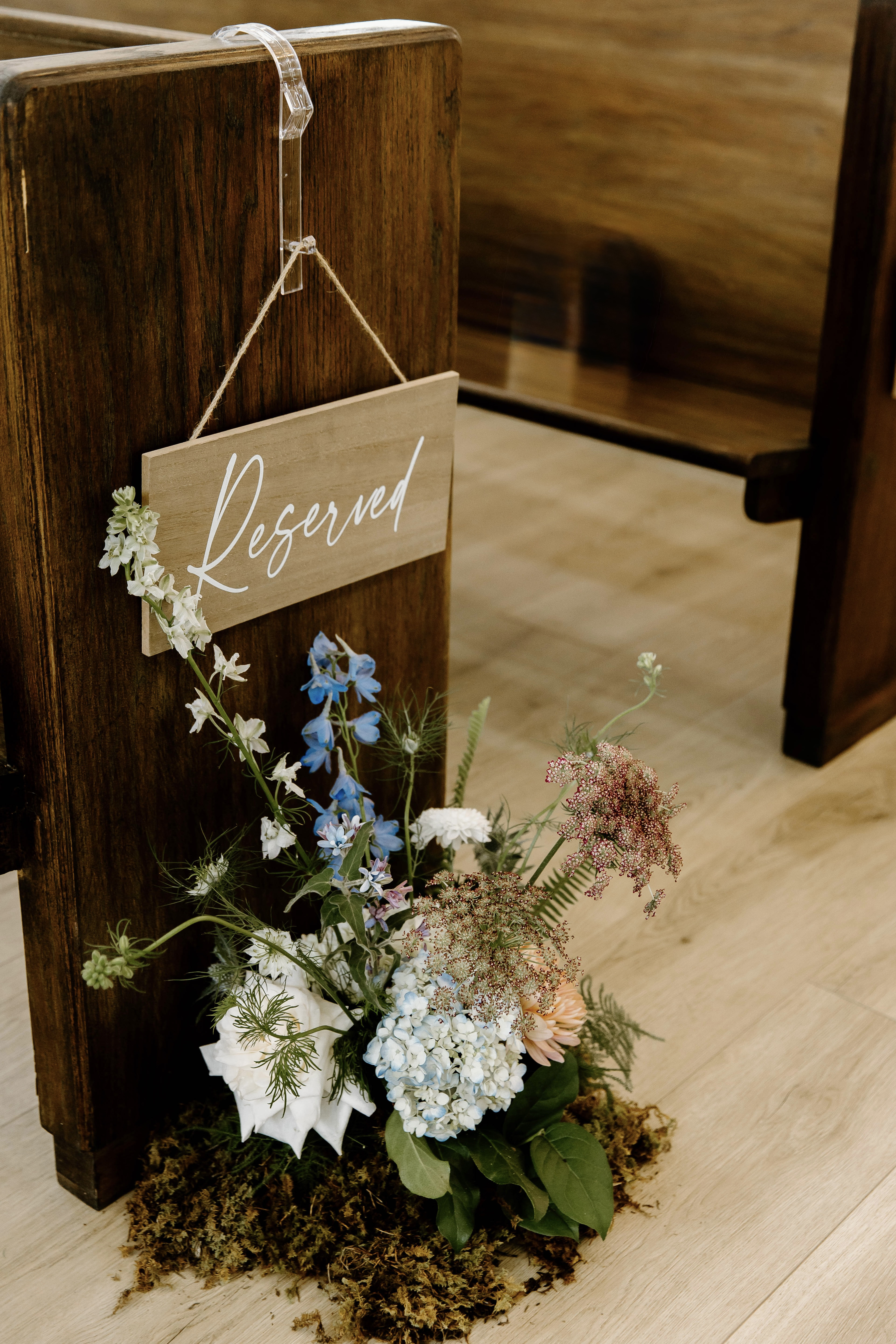 Blue and white flowers with moss at the base of a reserved chapel pew