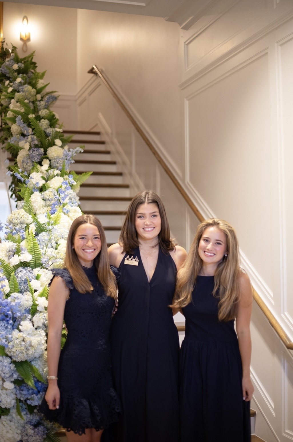 Three women standing beside the flower-covered staircase at the Tri Delt gathering