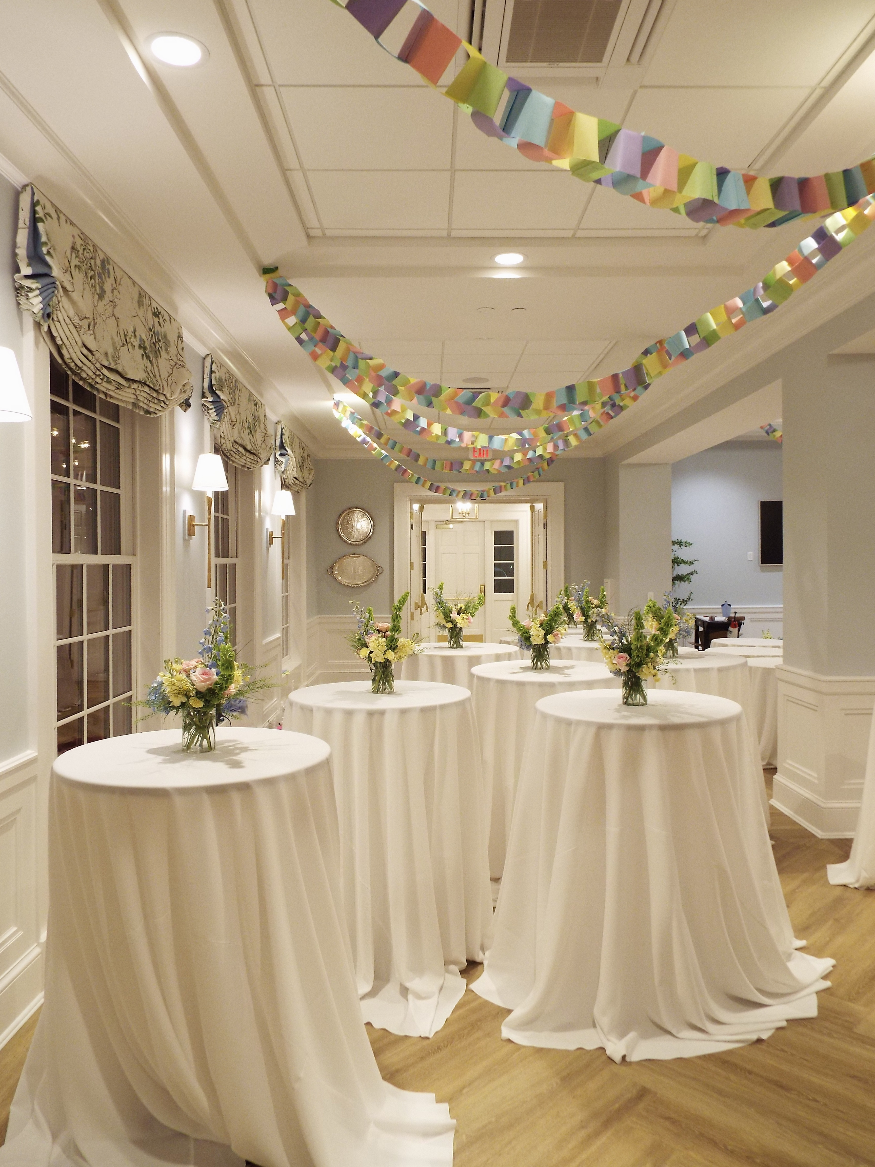 Multiple cocktail tables with pastel floral arrangements beneath colorful streamers at the Tri Delt gathering